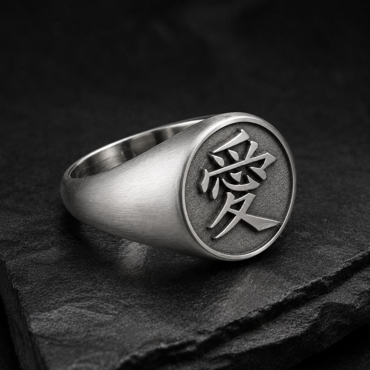A silver ring with a circular emblem featuring an Asian character, likely a symbol or deity, on a dark surface.