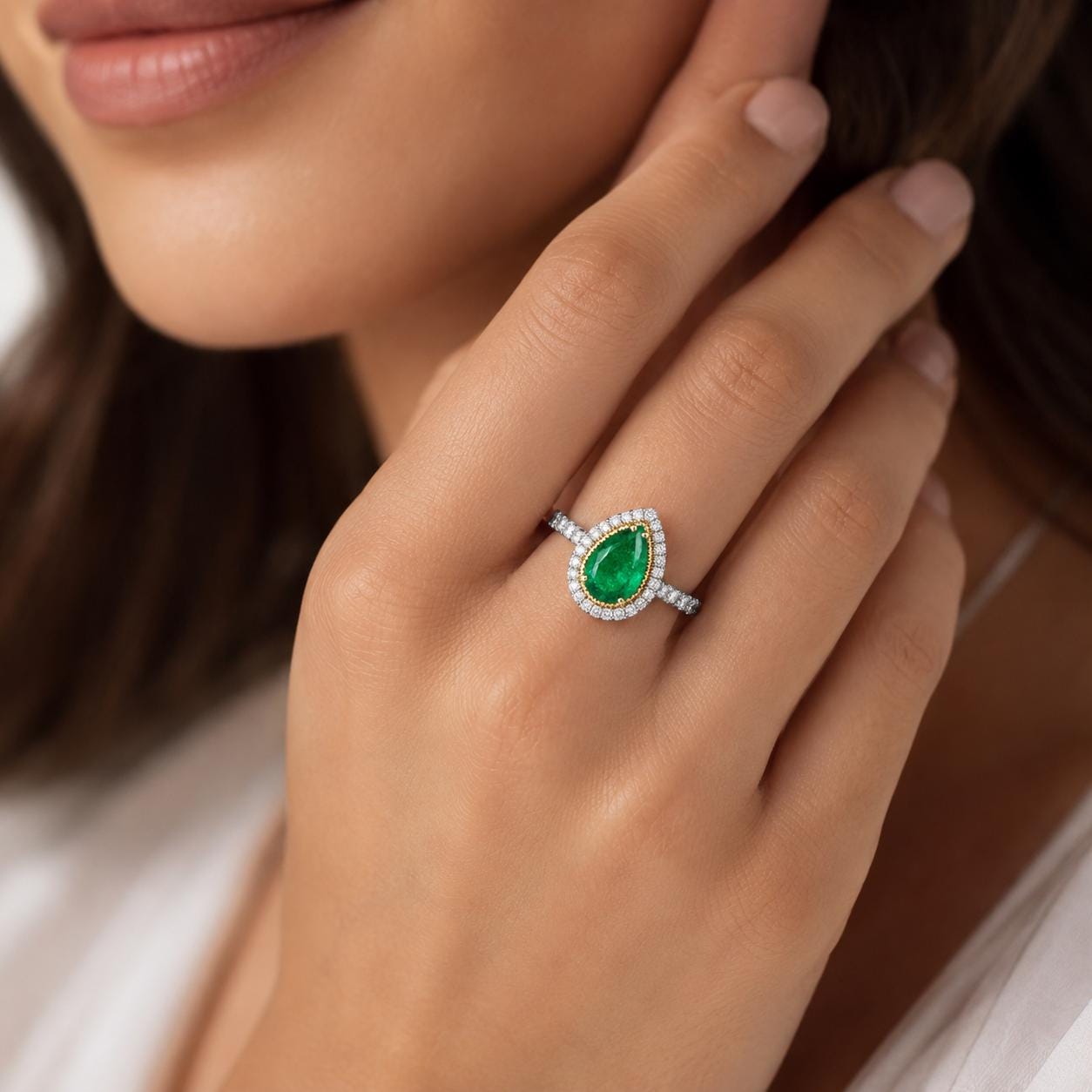 A close-up of a person's hand wearing a ring with a large, oval-shaped green gemstone surrounded by smaller diamonds.