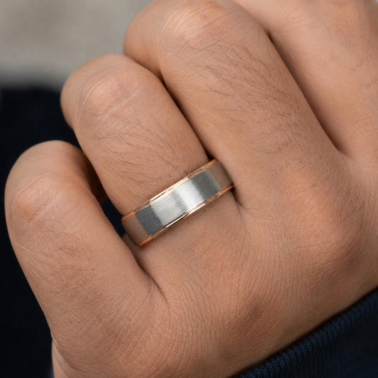 A close-up of a person's hand wearing a silver and gold wedding ring.