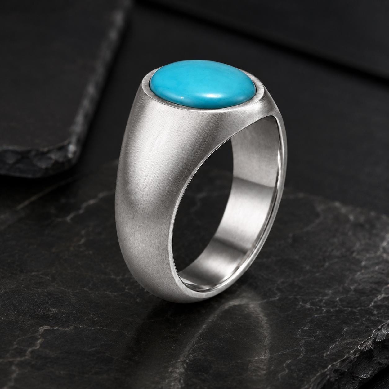 A silver ring with a turquoise stone set in the center, resting on a dark surface.