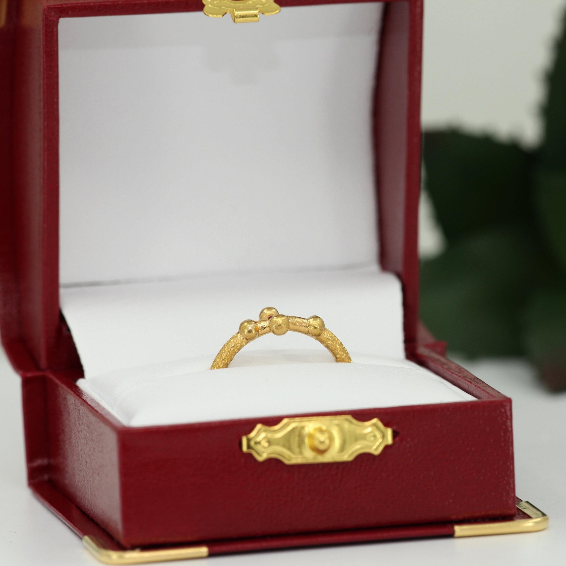 A gold ring is displayed in a red jewelry box with a white interior.