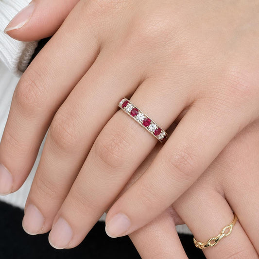 A close-up image of a person's hand wearing a ring with a row of red gemstones.