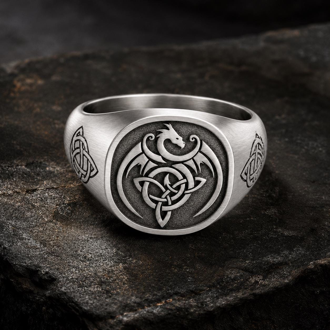 A silver ring with a dragon design and Celtic knot patterns.