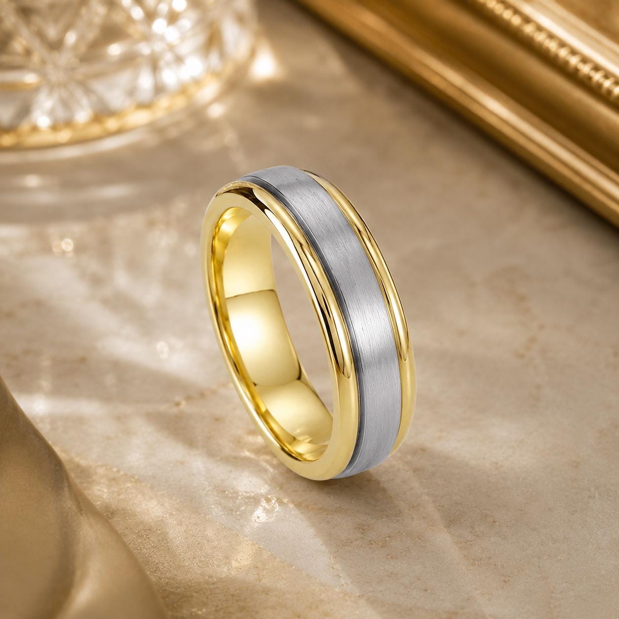A gold and silver wedding band with a metallic band and a thin gold band is displayed on a marble surface.