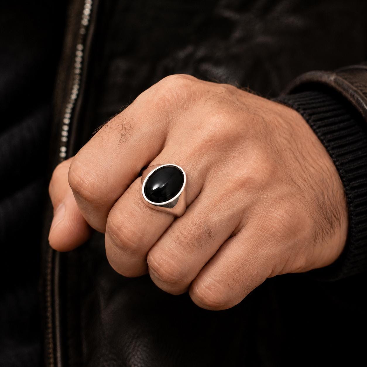 A close-up of a person's hand wearing a silver ring with a black stone.