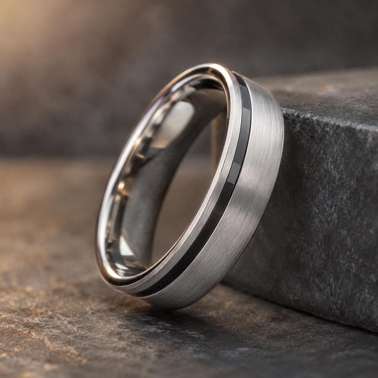 A silver ring with a black band is resting on a gray surface.