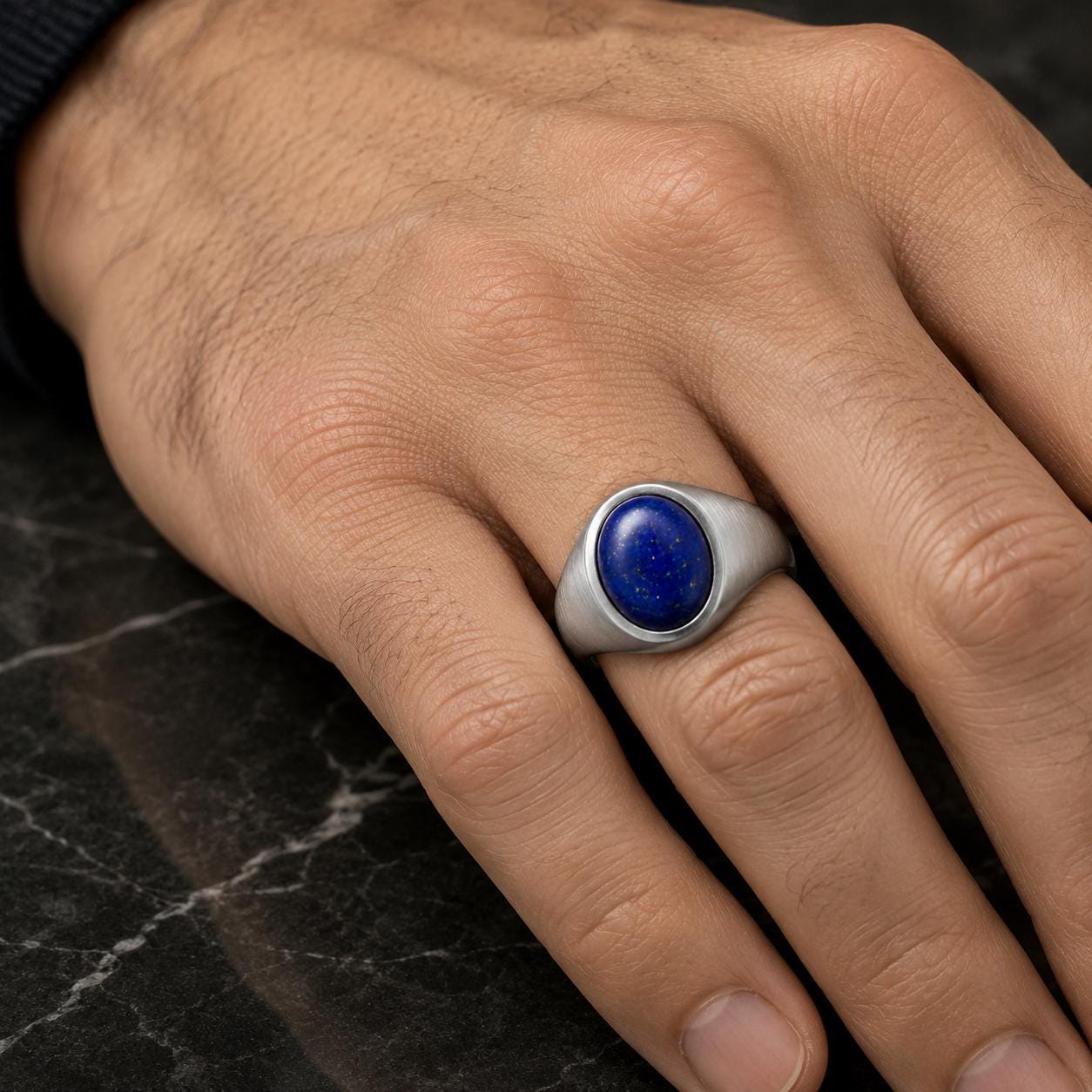 A close-up image of a hand wearing a silver ring with a blue lapis lazuli stone.
