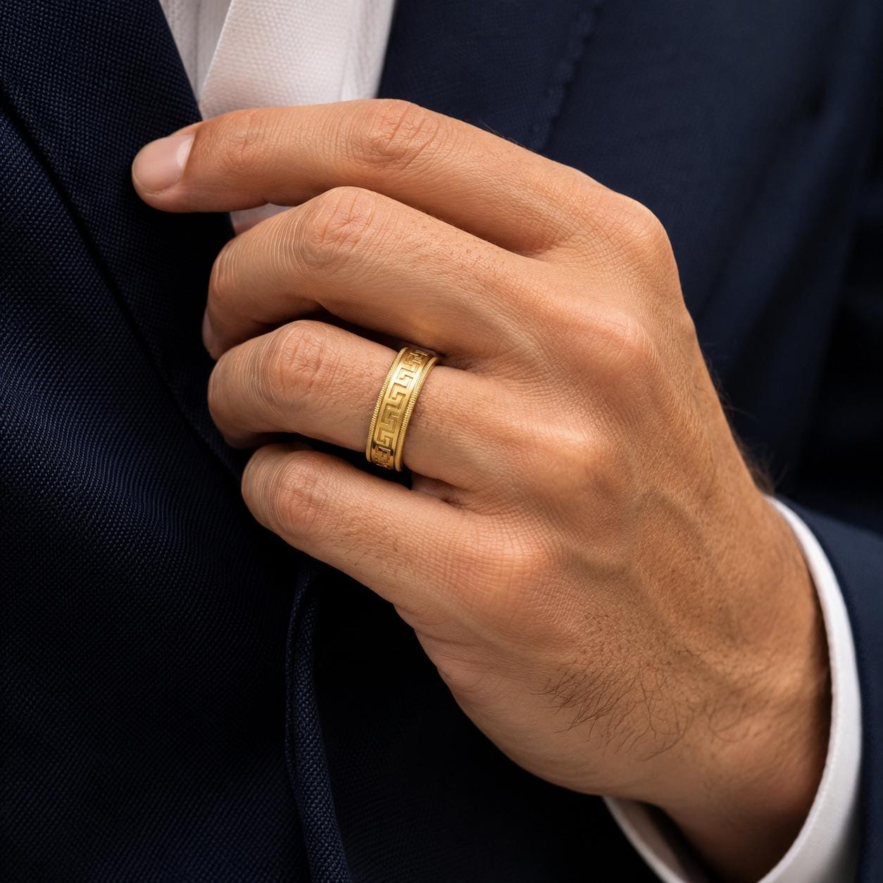 A close-up of a man's hand wearing a gold ring, with a dark suit jacket visible.
