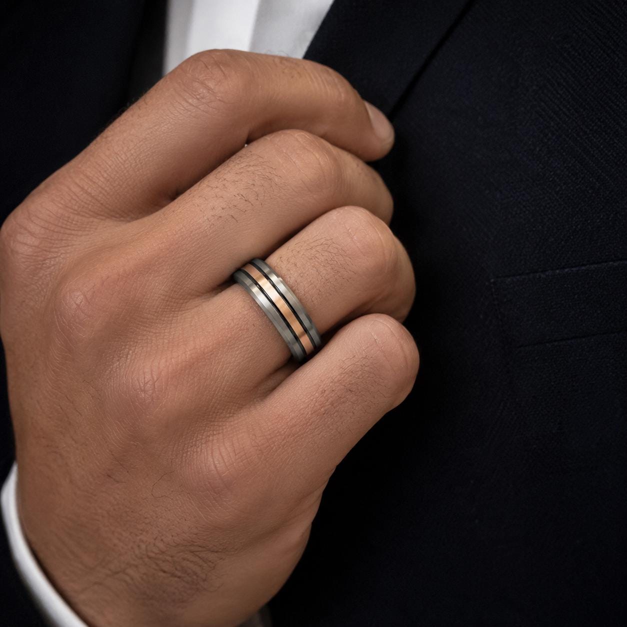 A close-up of a man's hand wearing a ring on the ring finger, with a black jacket visible in the background.