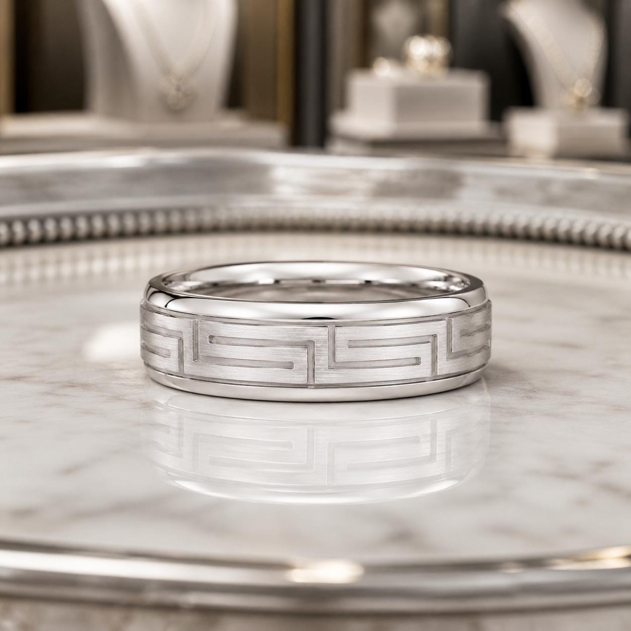 A silver ring with a geometric pattern sits on a marble surface.