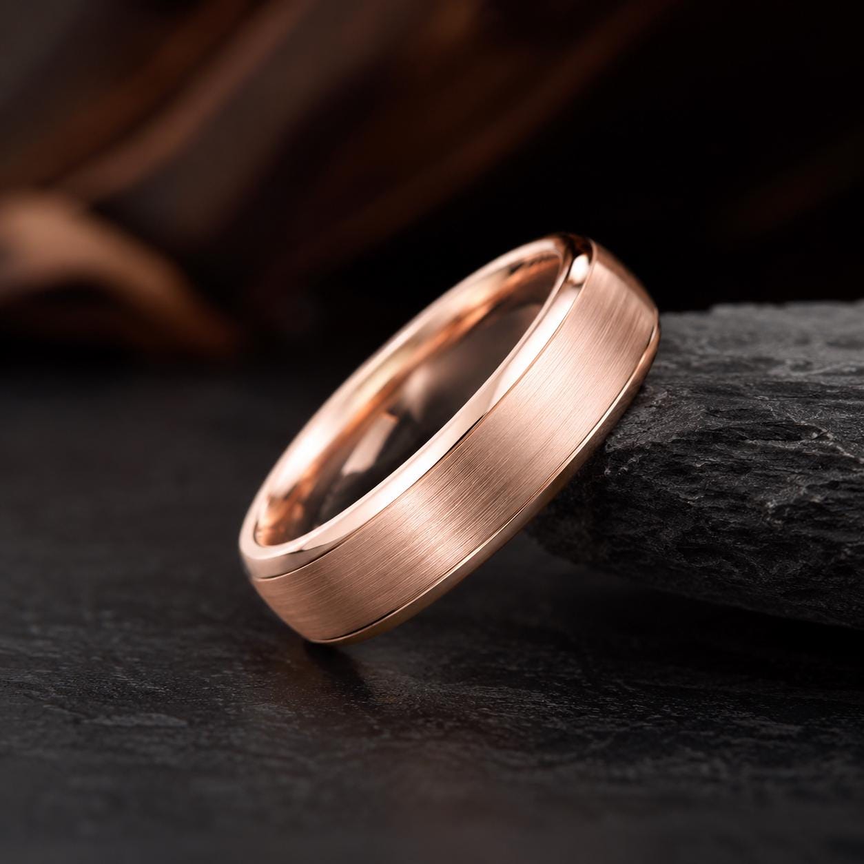 A gold-colored ring with a smooth, polished surface rests on a dark surface, creating a striking contrast.