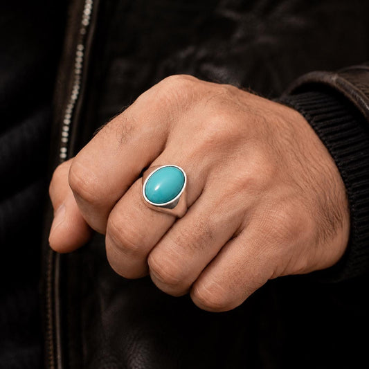 A close-up of a person's hand wearing a turquoise stone ring.