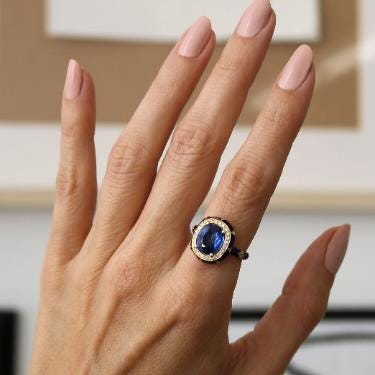 A close-up of a hand wearing a ring with a blue gemstone.