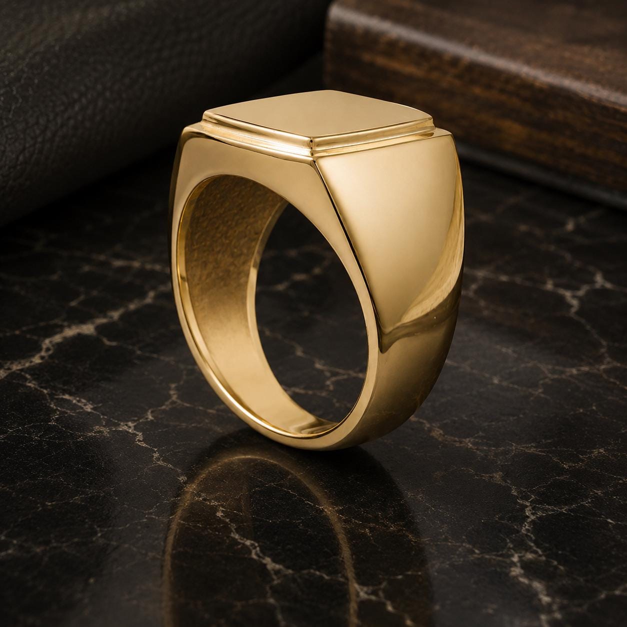 A gold ring with a square-shaped gemstone is displayed on a dark marble surface.