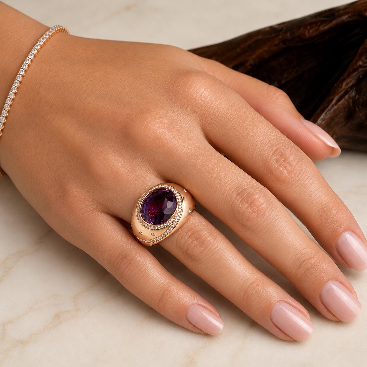 A close-up image of a hand wearing a gold ring with a large purple gemstone, resting on a marble surface.