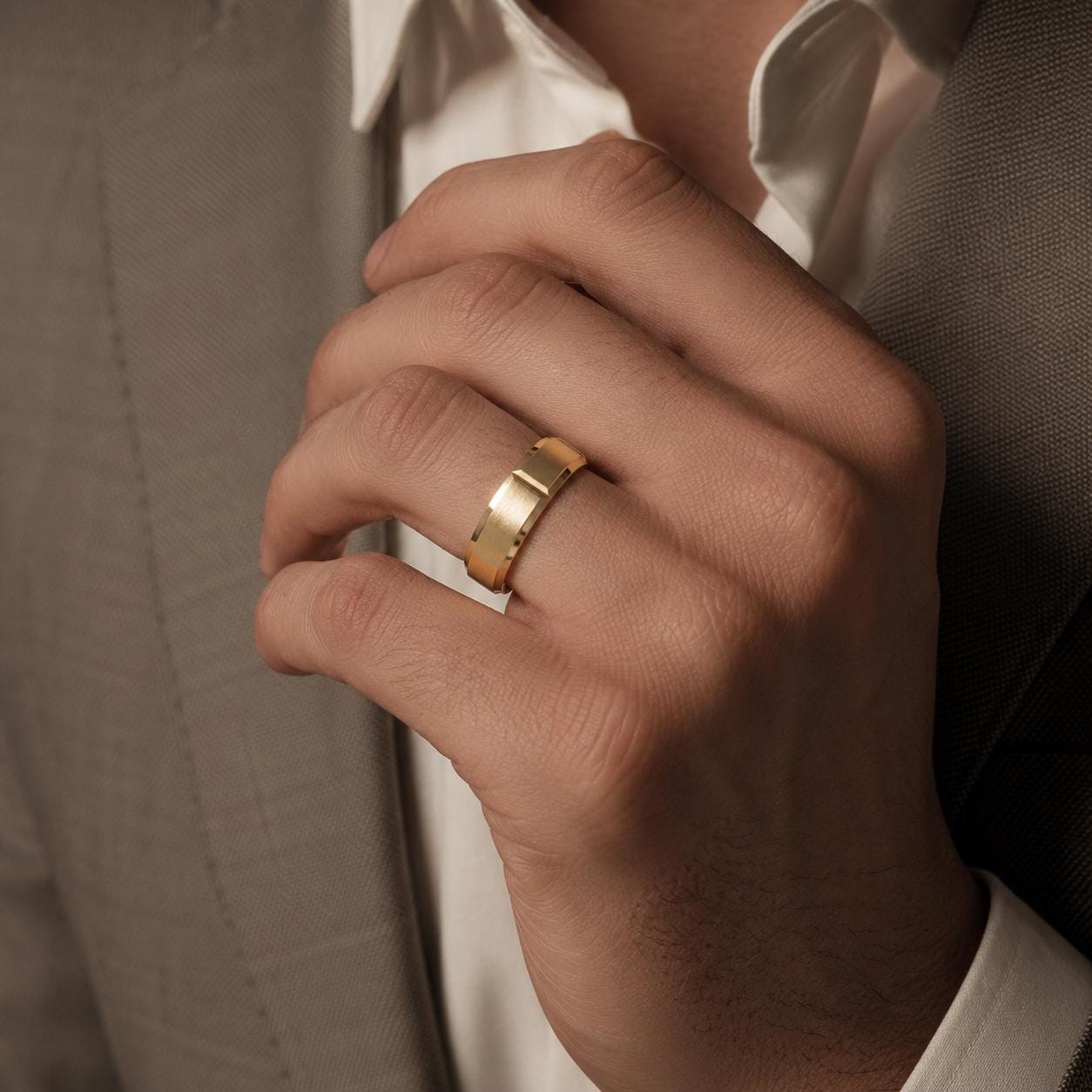 A close-up of a person's hand wearing a gold ring, with a suit jacket visible in the background.