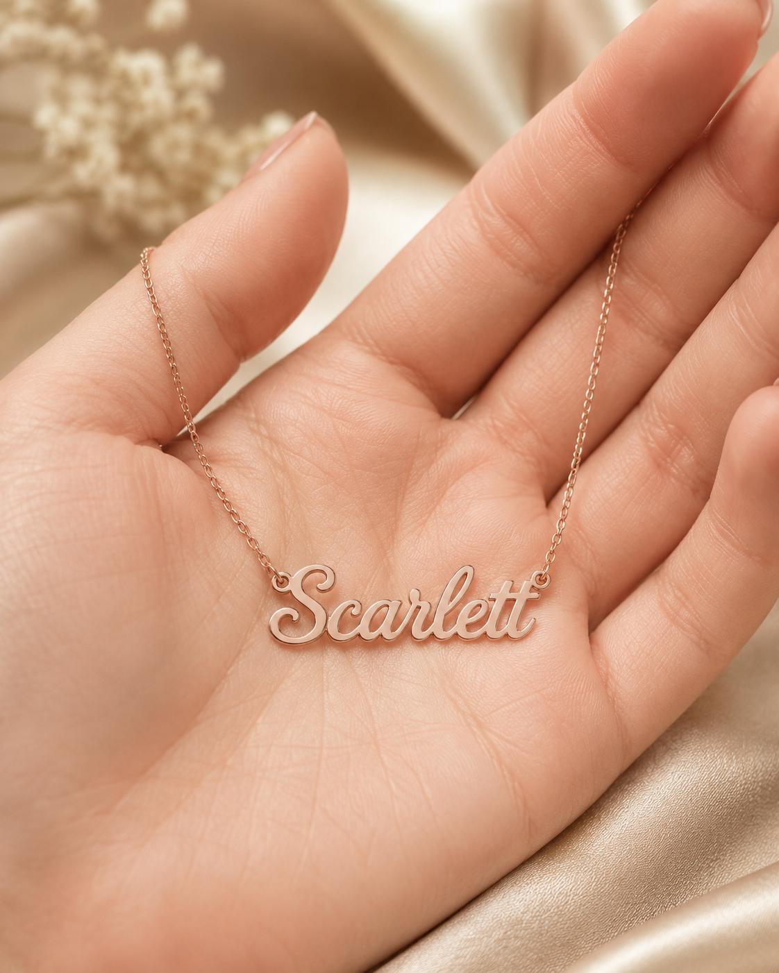 A hand holding a necklace with the name "Scarfett" engraved on it.