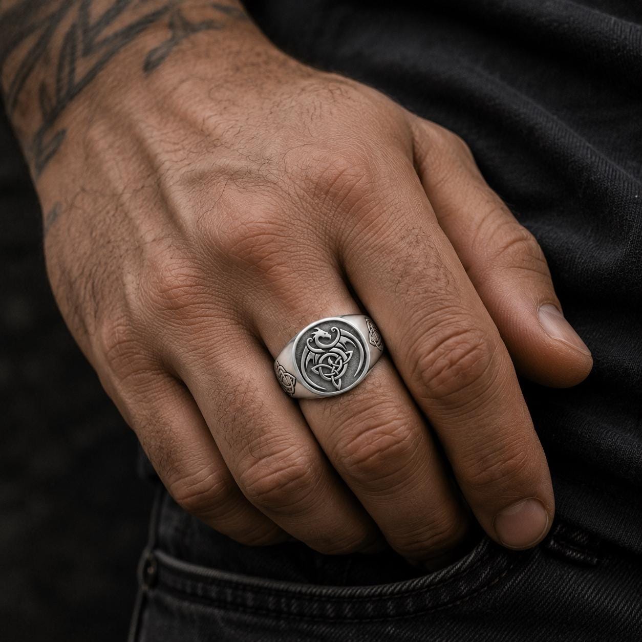 A close-up of a person's hand wearing a silver ring with a design on it.