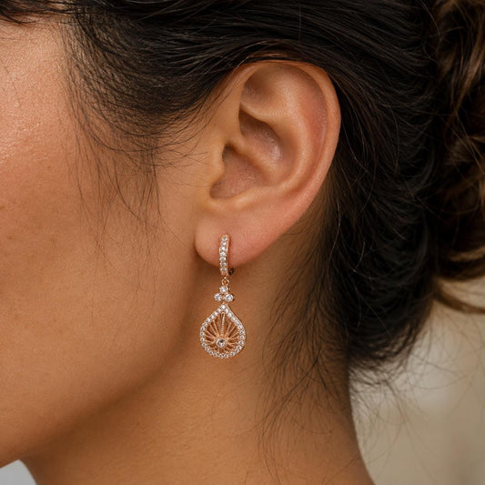 A close-up view of a woman's ear adorned with a delicate gold earring featuring a leaf-shaped design and sparkling gemstones.