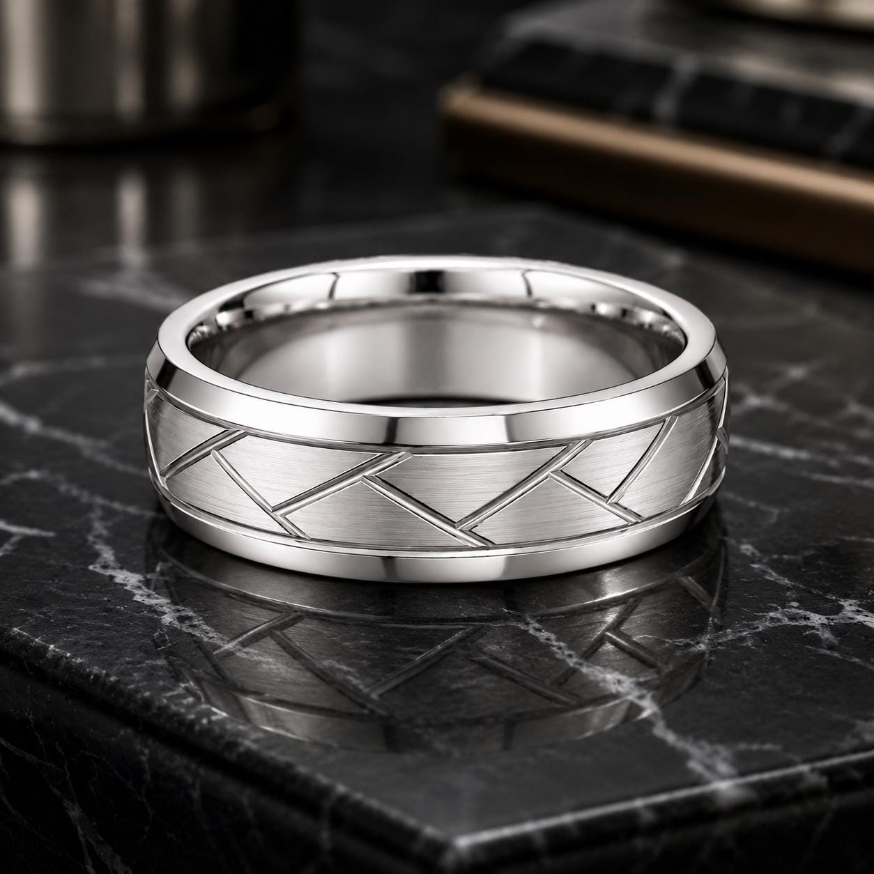 A silver ring with a geometric pattern sits on a black marble surface.