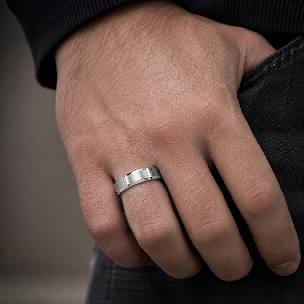 A close-up of a person's hand wearing a silver ring on the ring finger.