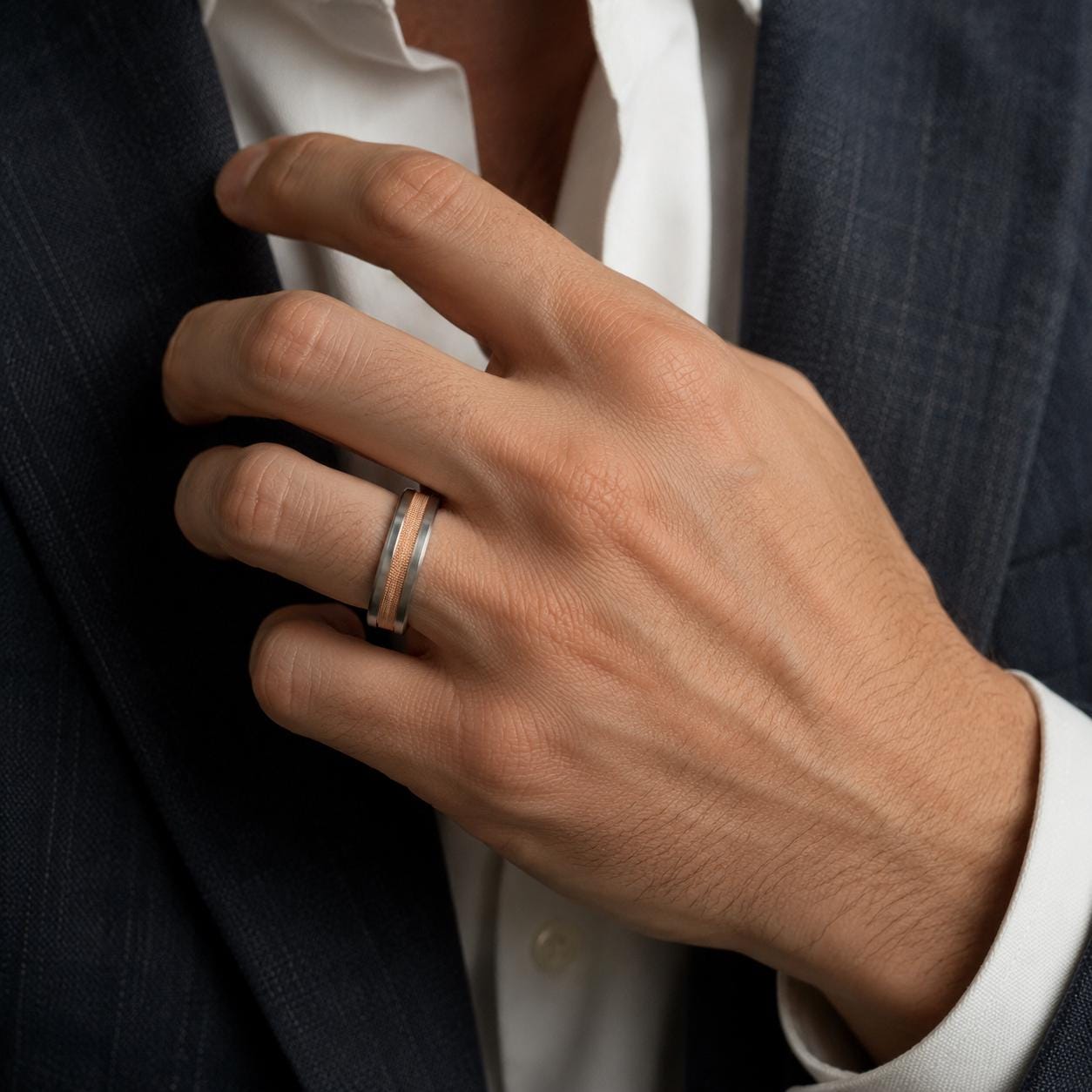 A close-up of a man's hand wearing a ring, with a suit jacket visible in the background.