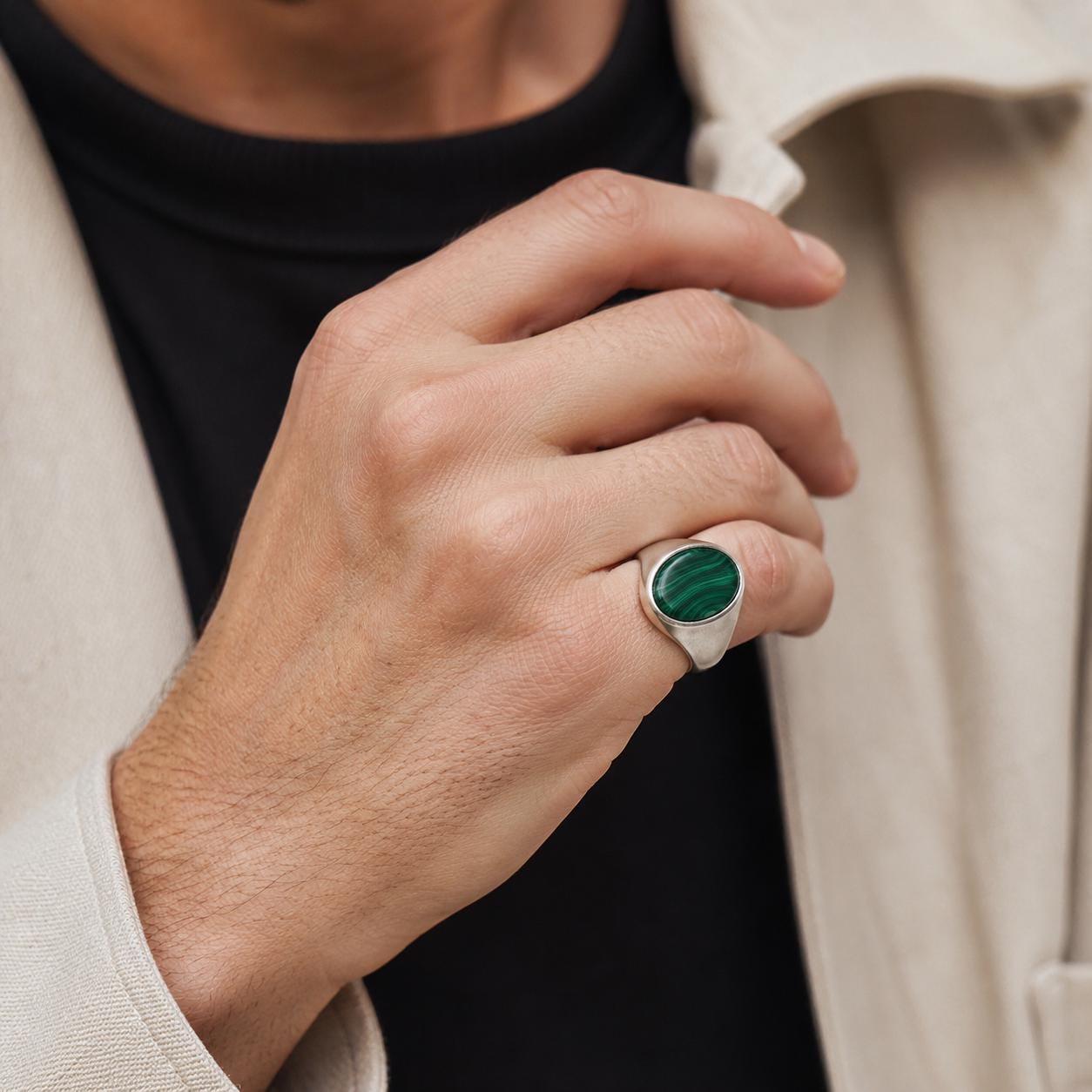 A close-up of a person's hand wearing a silver ring with a green gemstone.
