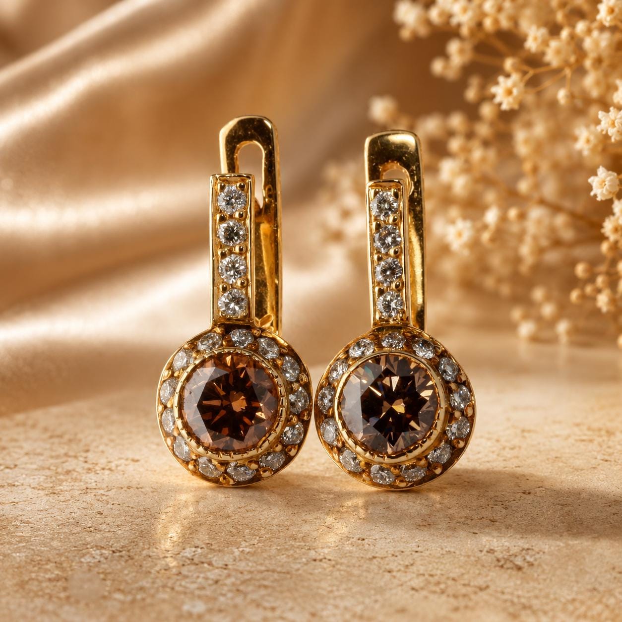A pair of gold earrings with large, round gemstones set in a halo-like design, placed on a beige background.