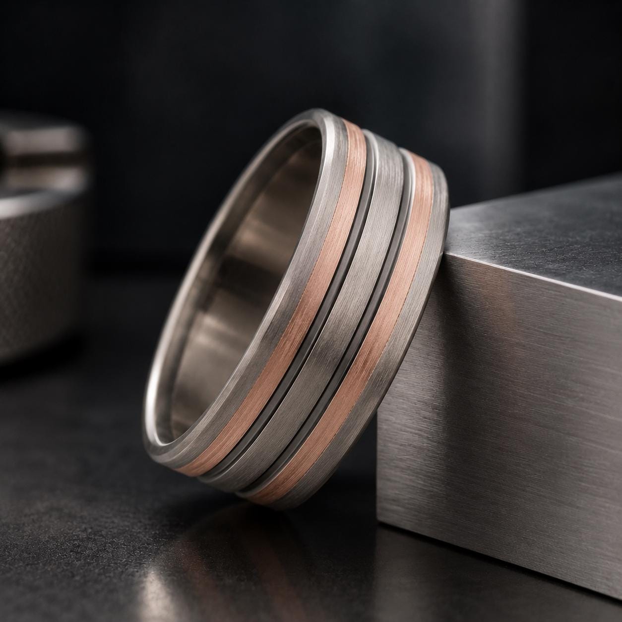 A silver ring with three concentric bands of different colors, including silver, copper, and gold, is resting on a metallic surface.