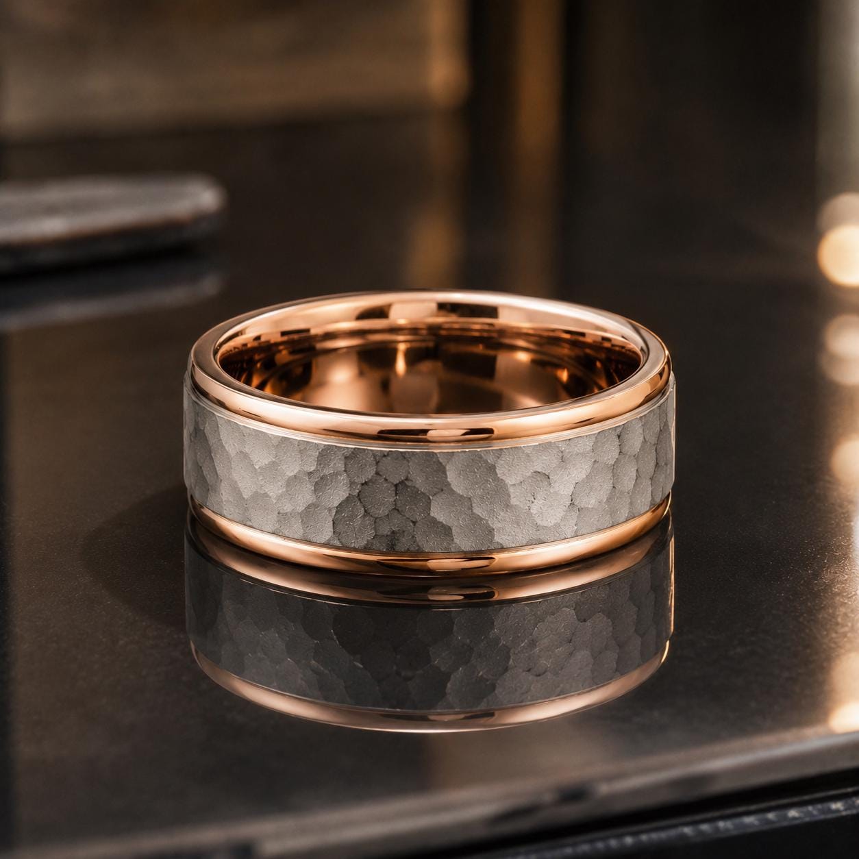 A gold and silver ring with a textured surface sits on a reflective surface, creating a visually appealing contrast.