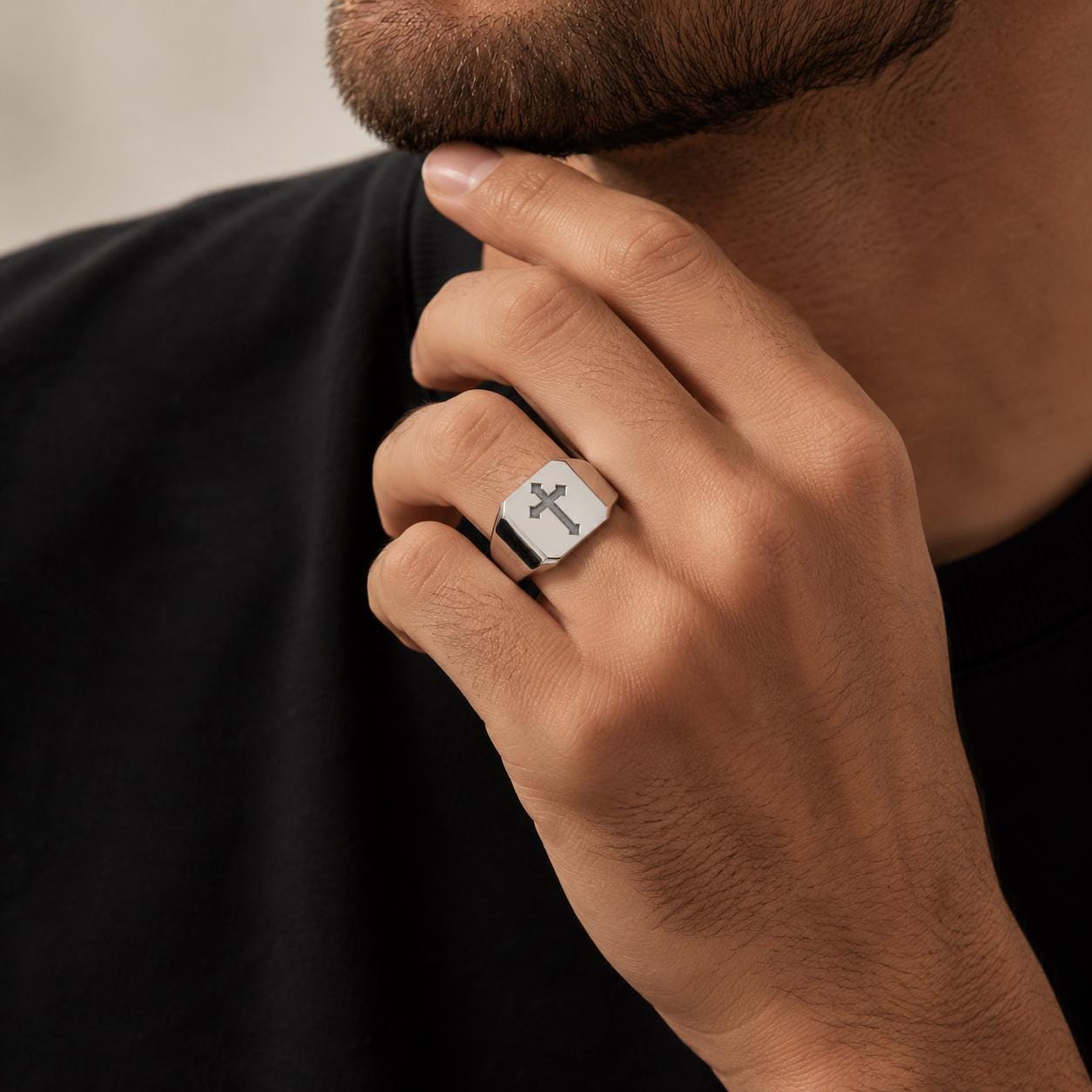 A close-up of a person's hand wearing a silver ring with a cross symbol on it.