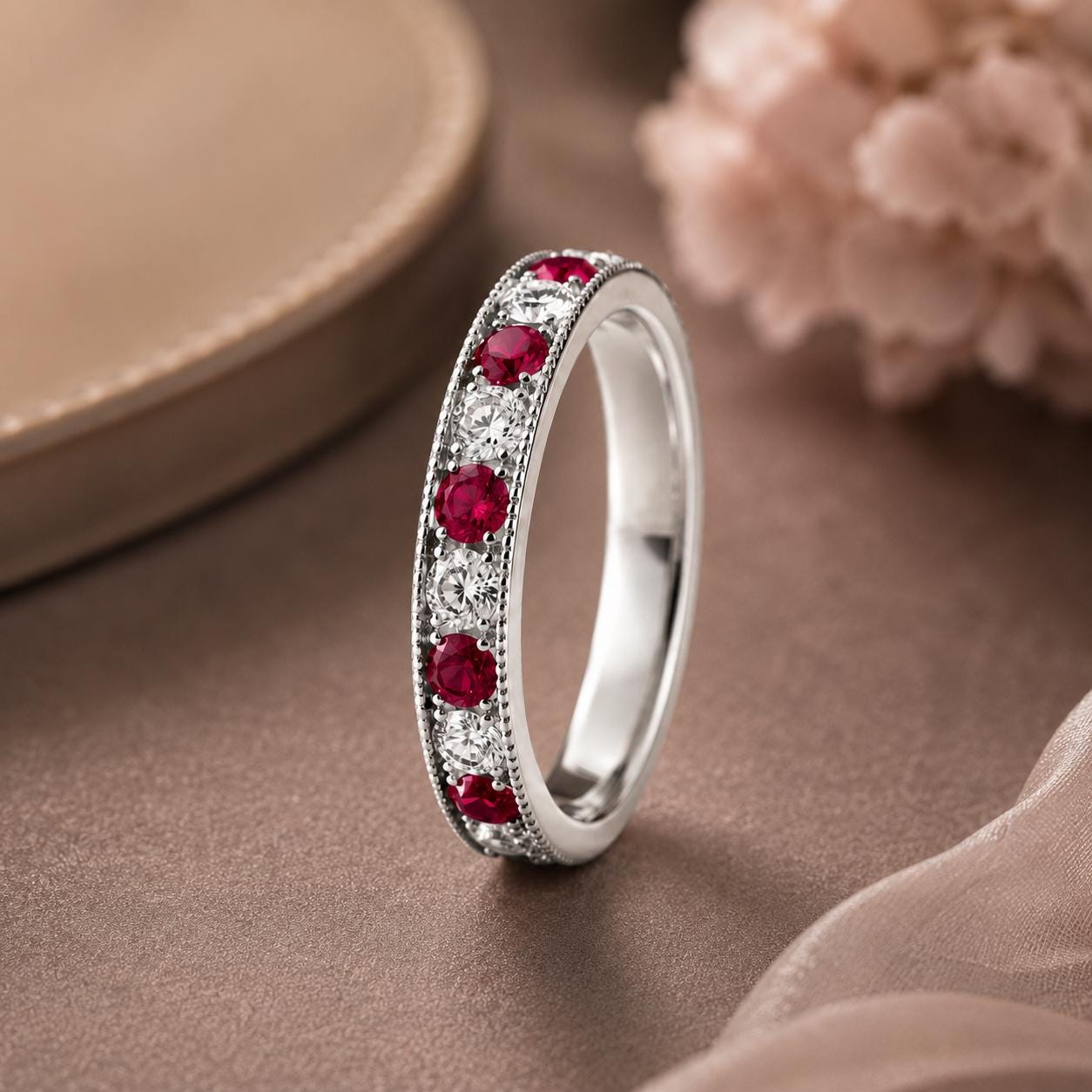 A silver ring adorned with red gemstones, including diamonds, is displayed on a brown surface.