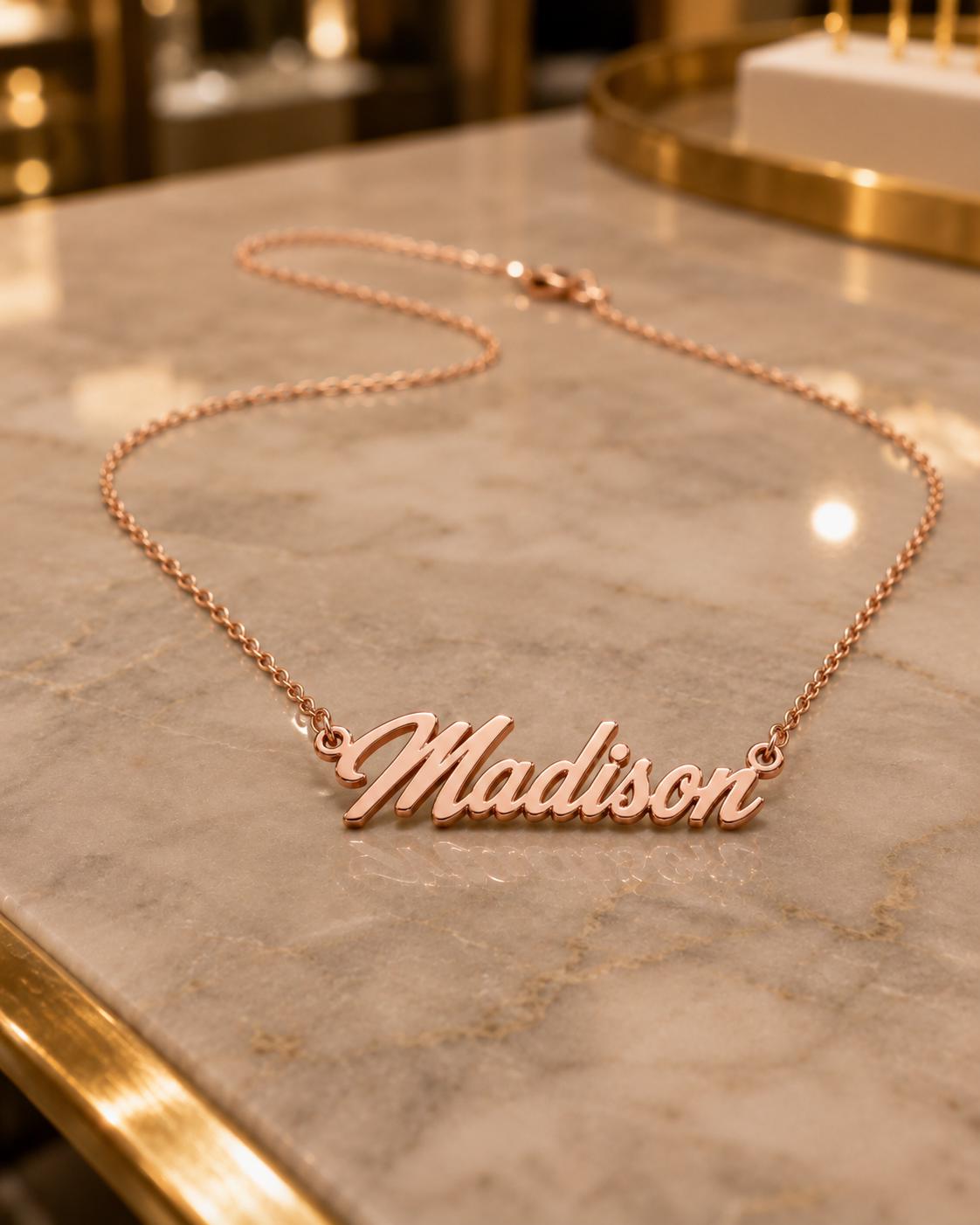 A necklace with the name "Madison" engraved on it, resting on a marble surface.