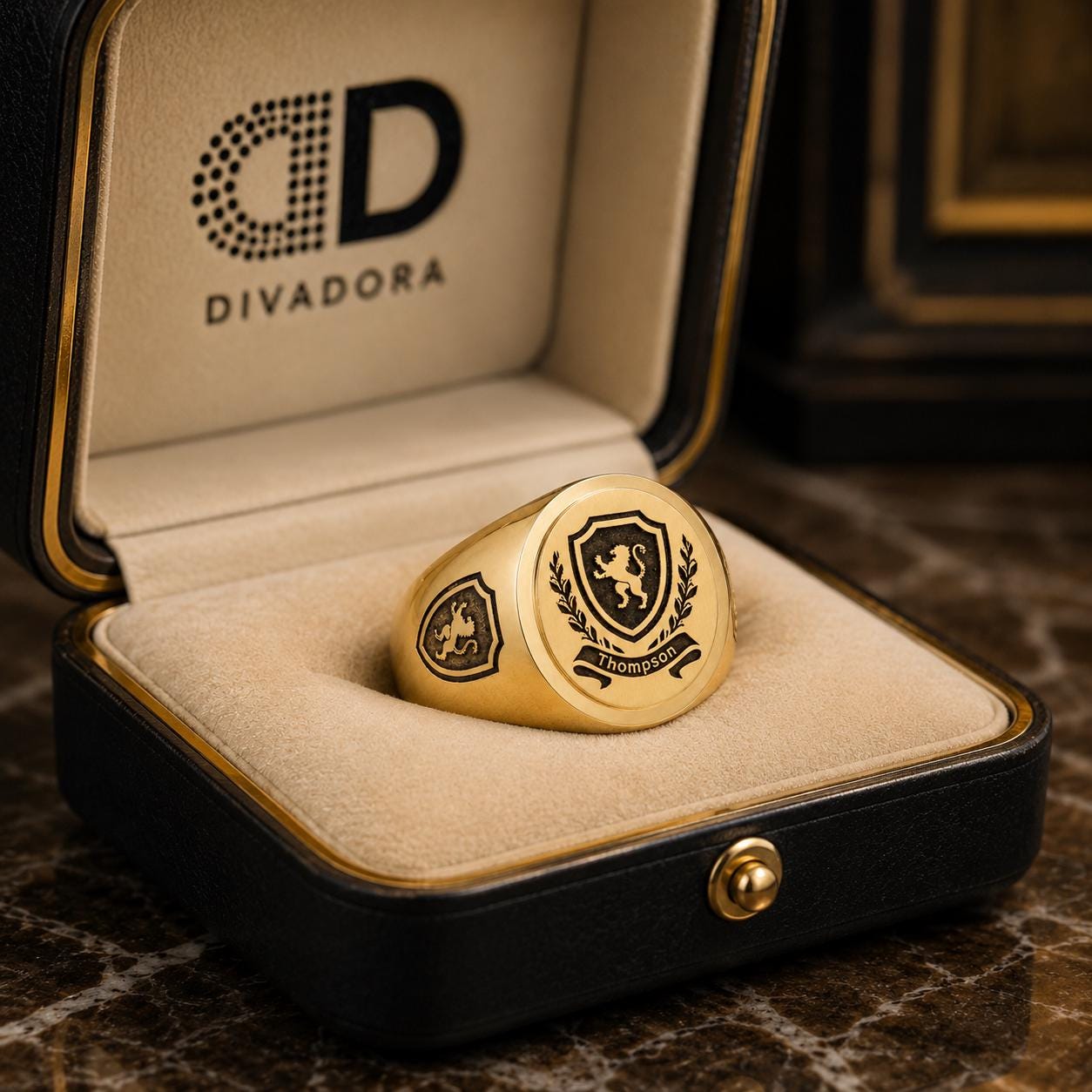 A gold ring with a shield design and the word "THOMPSON" engraved on it, placed in a black jewelry box with the Divador logo visible.