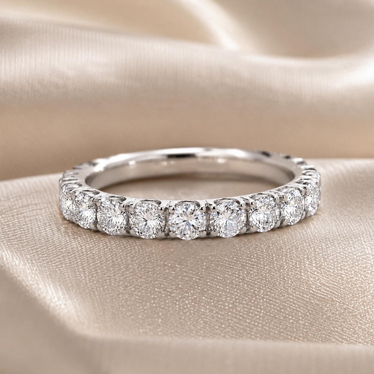 A diamond-encrusted ring with a row of round diamonds set in a silver band, resting on a beige fabric background.