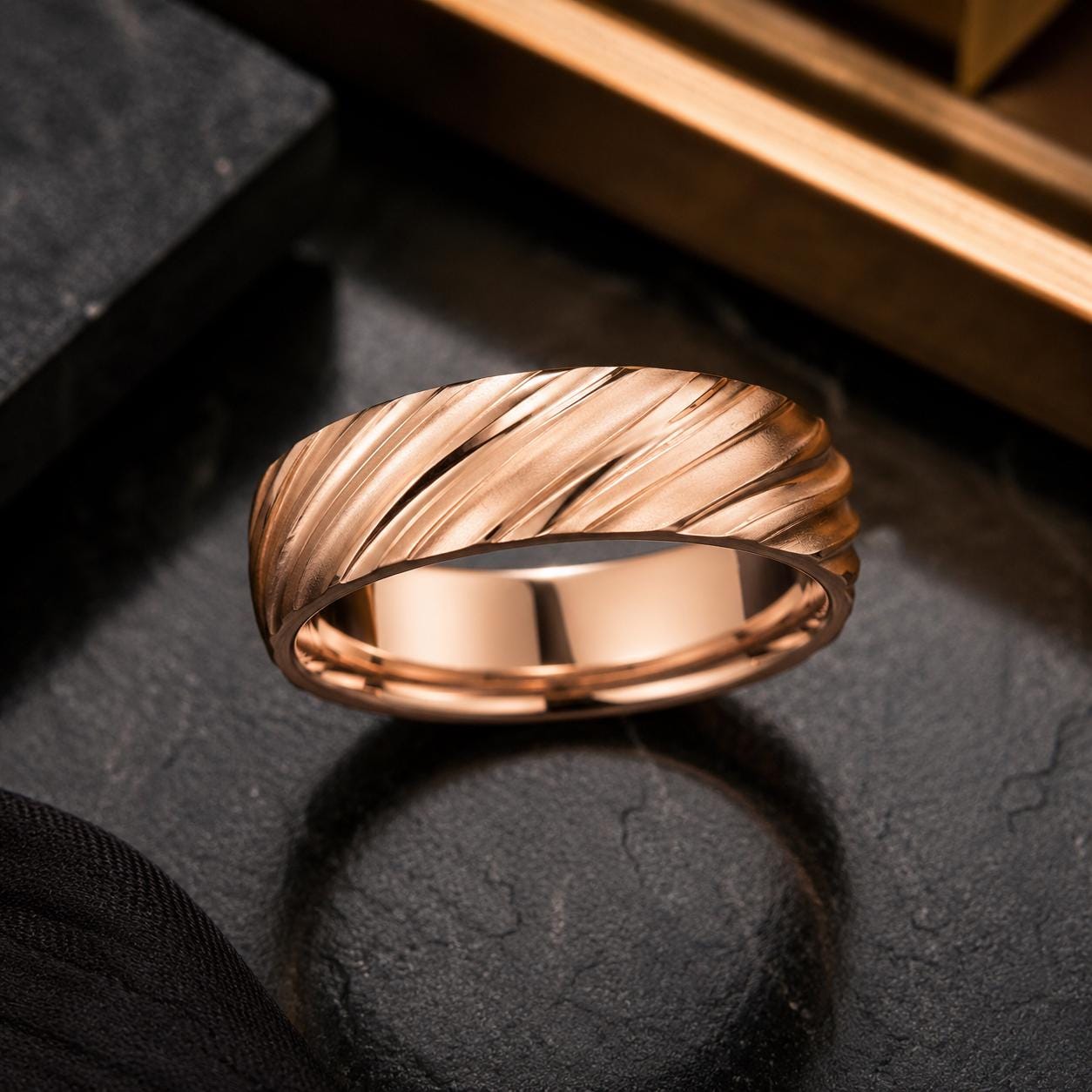 A gold ring with a twisted design sits on a dark surface, casting a shadow.