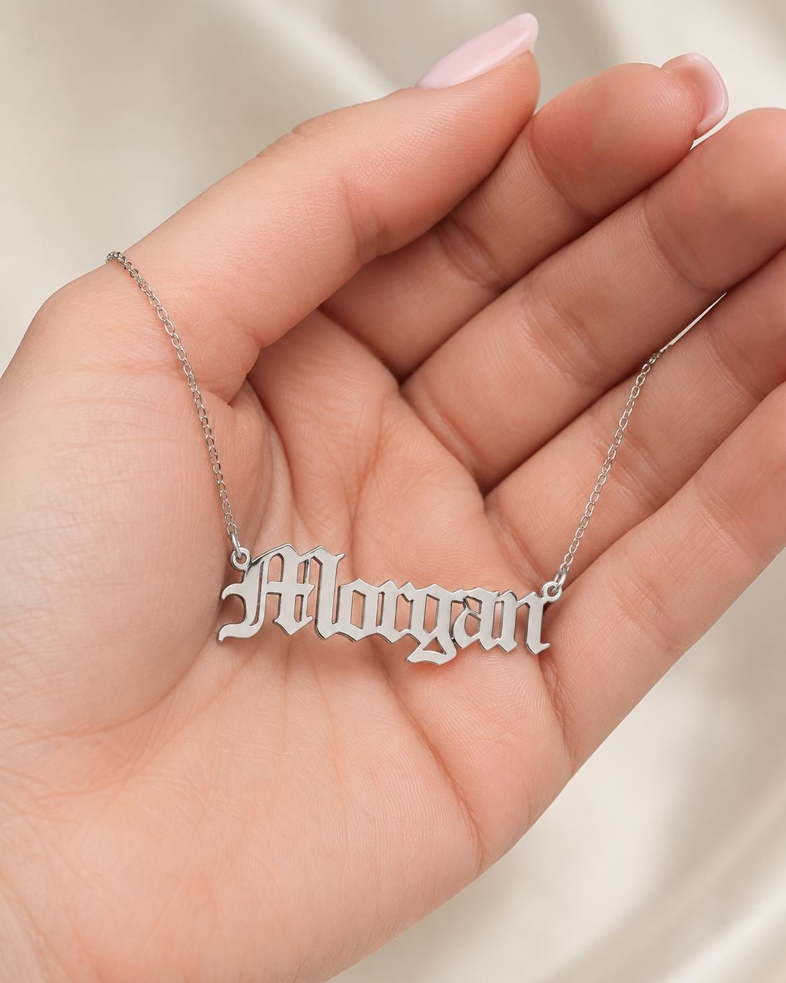 A hand holding a necklace with the name "Molly" engraved on it.