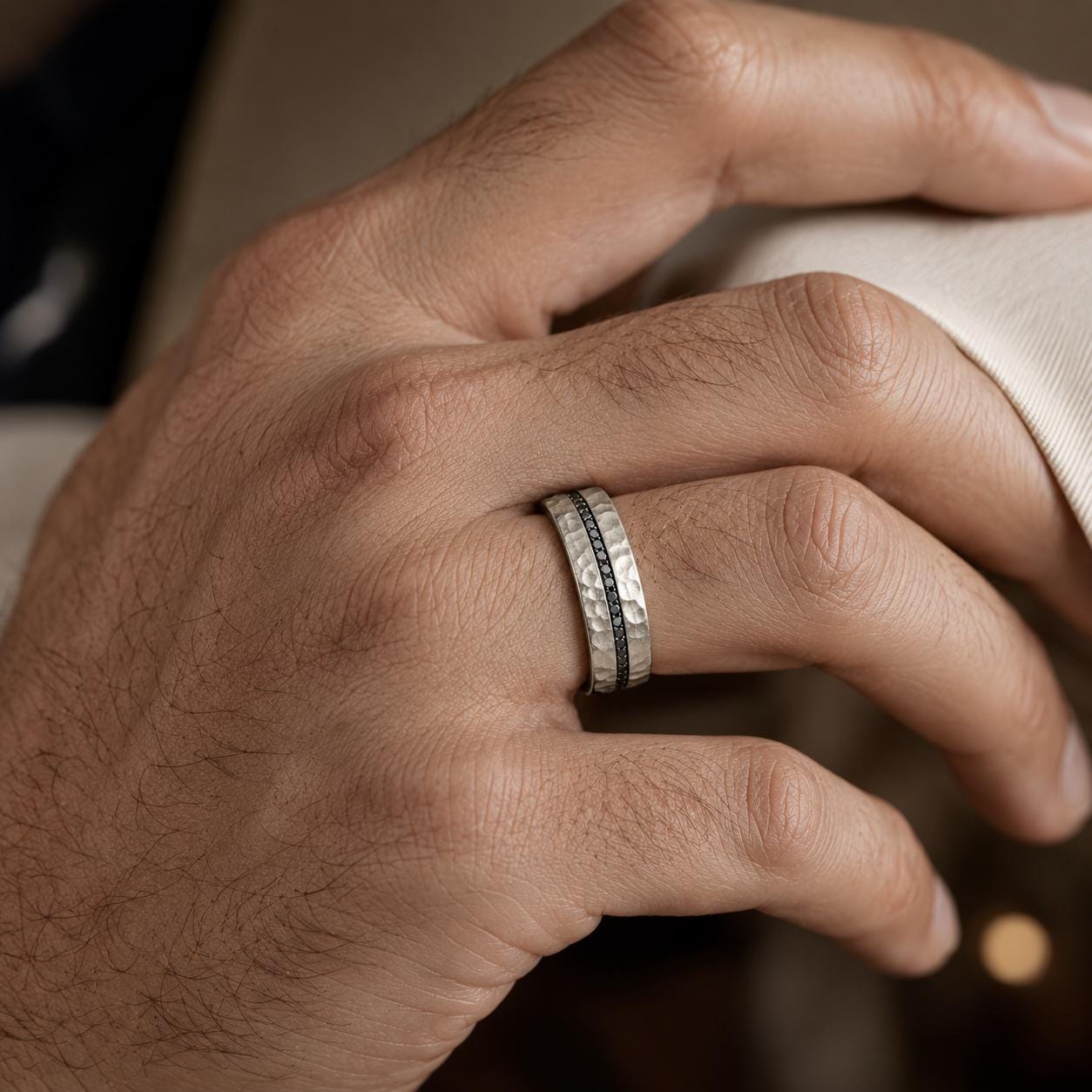 A close-up of a person's hand wearing a silver ring with a black band.