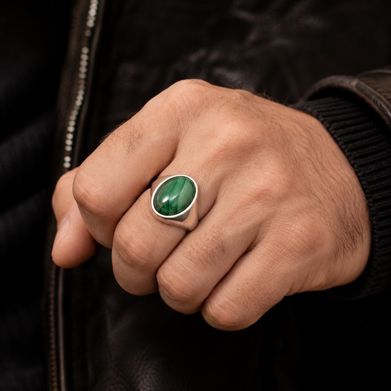 A close-up of a person's hand wearing a ring with a green gemstone.