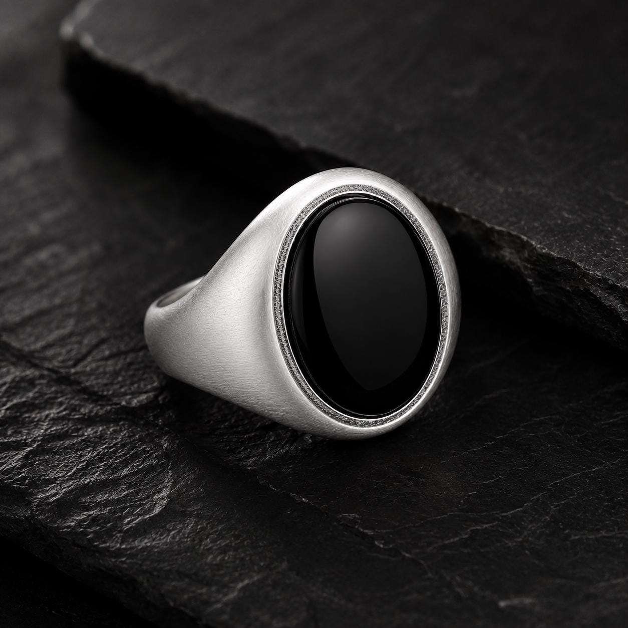 A silver ring with a black oval stone is displayed on a dark surface.
