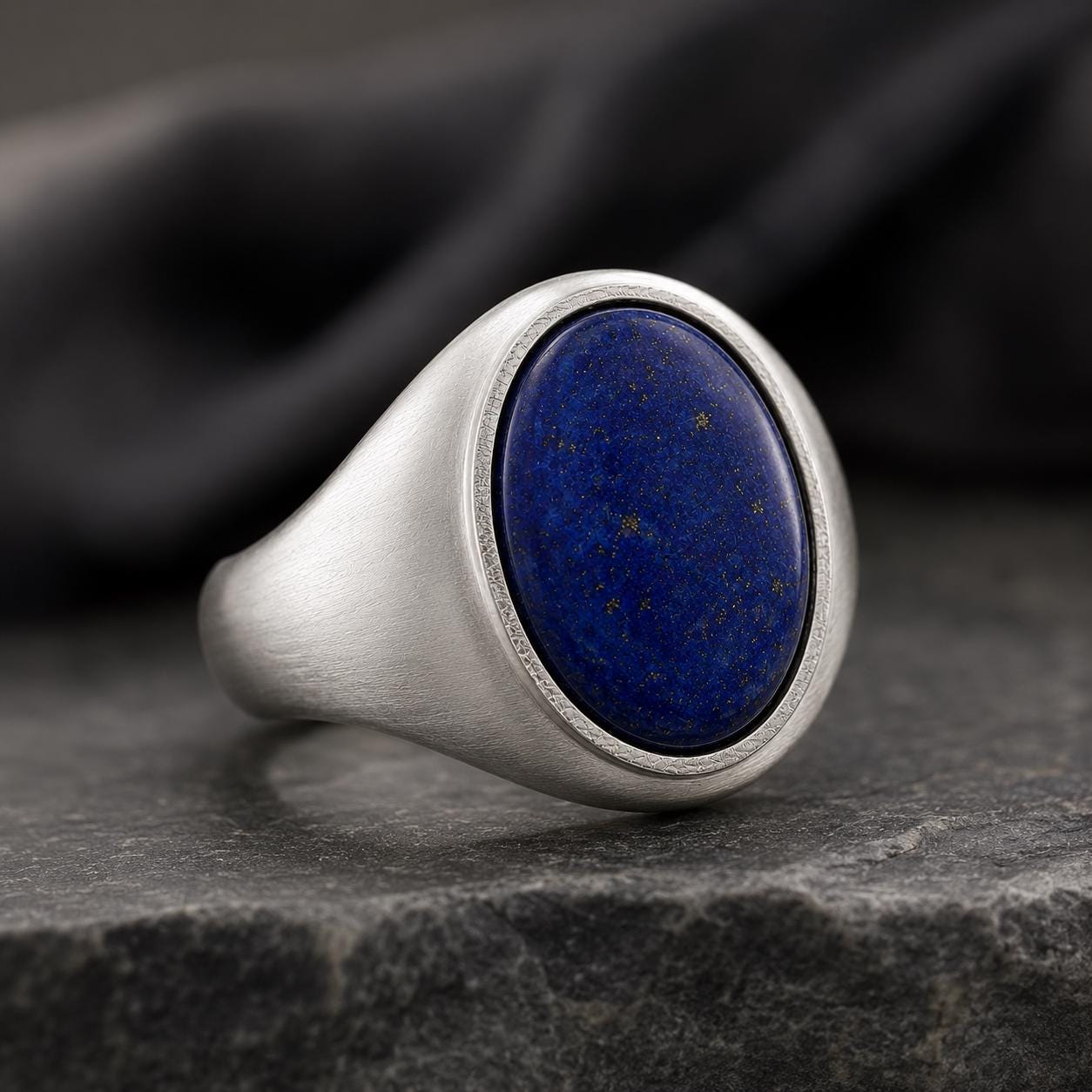 A silver ring with a large oval-shaped lapis lazuli stone set in the center, resting on a gray surface.