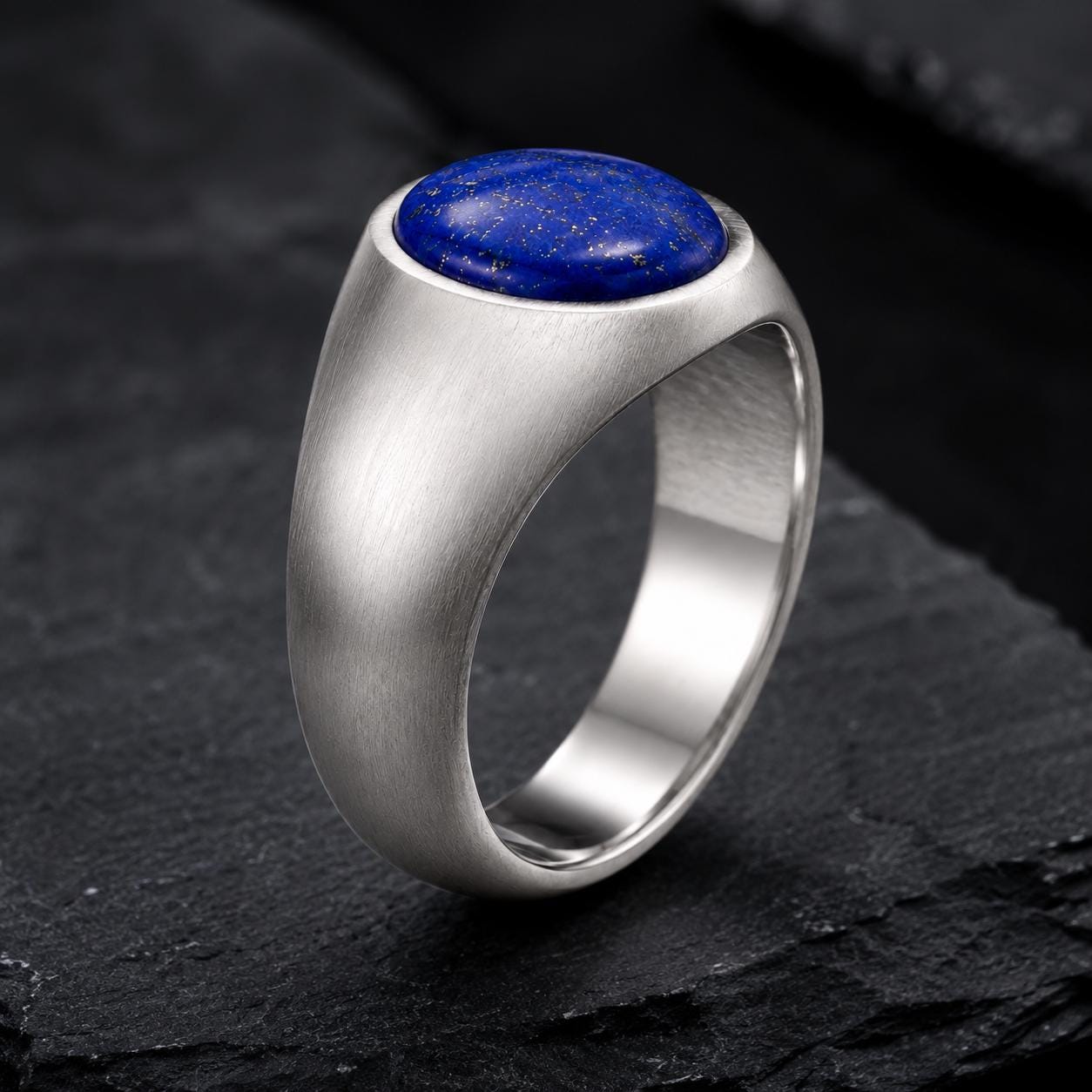 A silver ring with a blue lapis lazuli stone set in the center, resting on a dark surface.