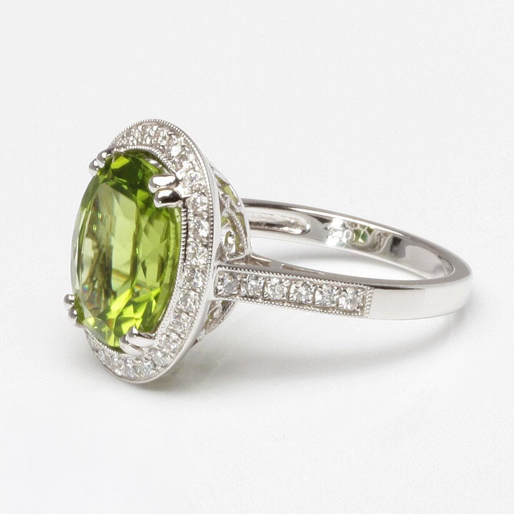 A silver ring with a large oval-shaped green gemstone, surrounded by smaller diamonds.