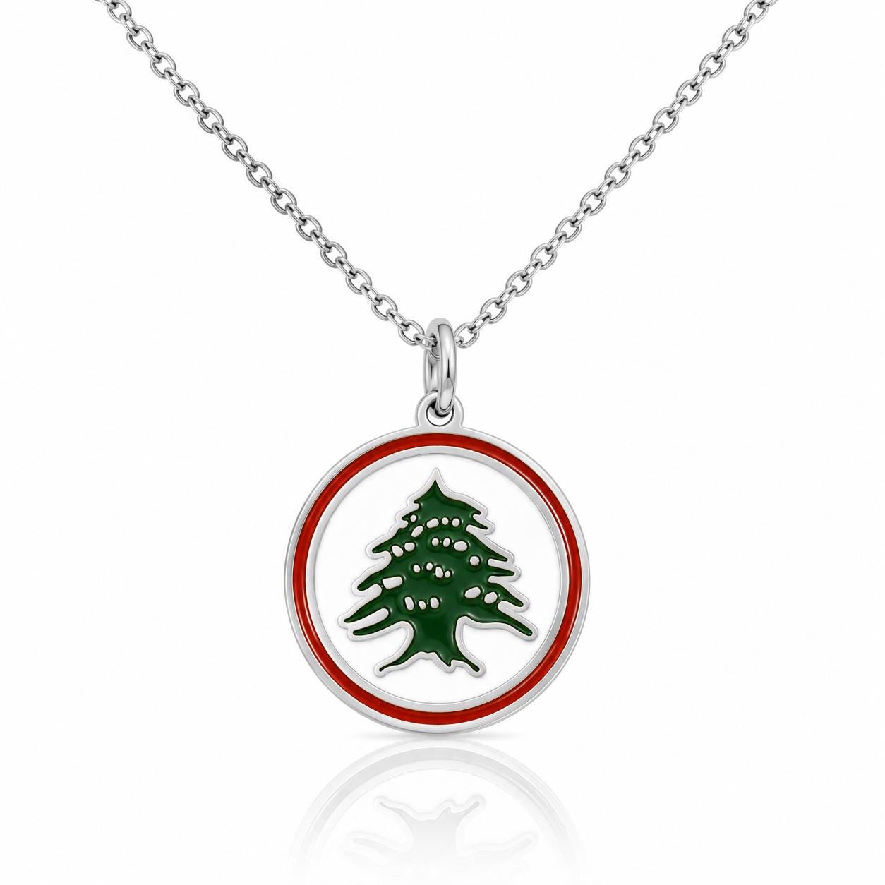 A silver necklace pendant with a circular design featuring a green tree with white or red leaves.
