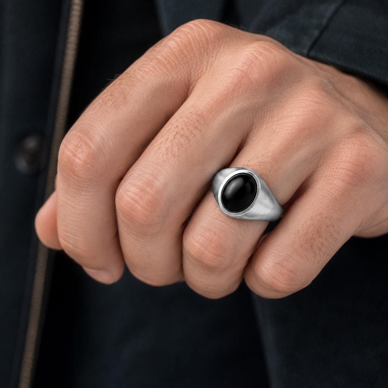A close-up of a person's hand wearing a silver ring with a black oval stone.