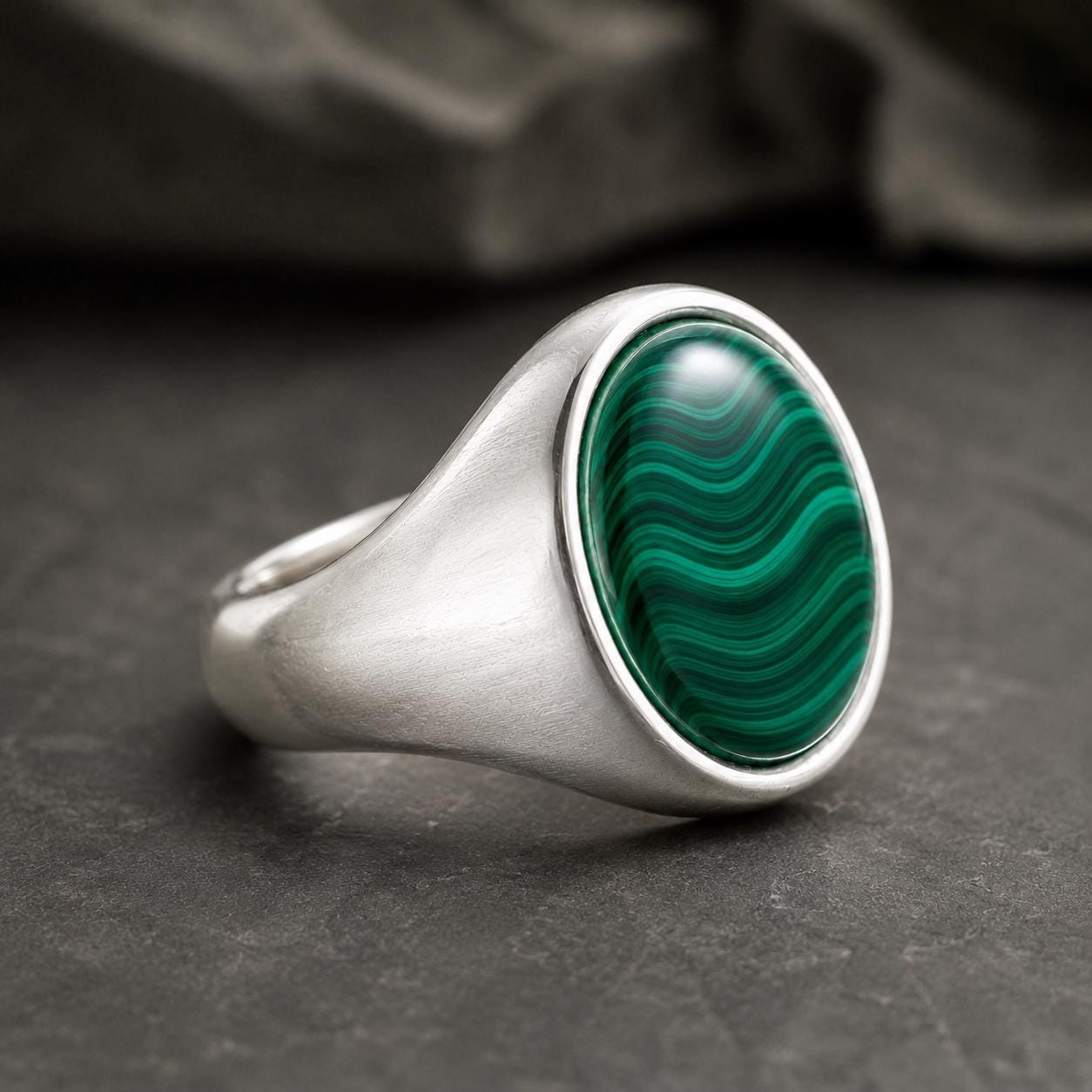 A silver ring with a large oval-shaped gemstone in the center, resting on a dark surface.