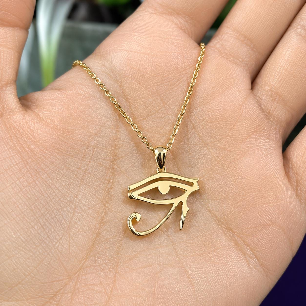 A gold-colored pendant necklace with a large eye symbol is being held in a person's hand.
