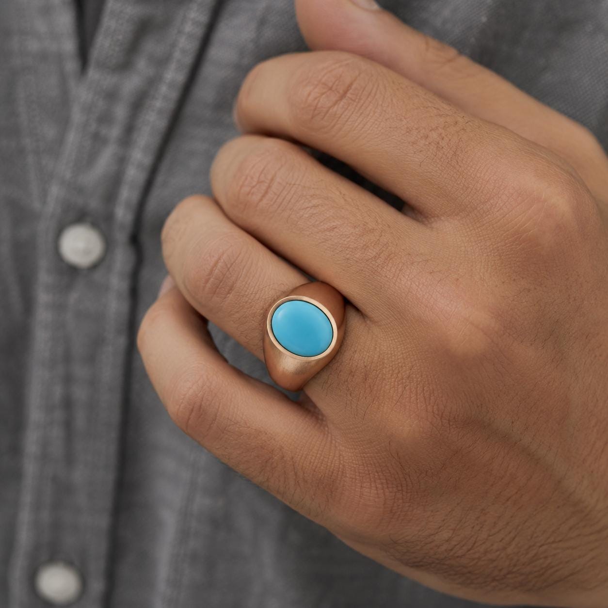 A close-up of a person's hand wearing a gold ring with a turquoise stone.