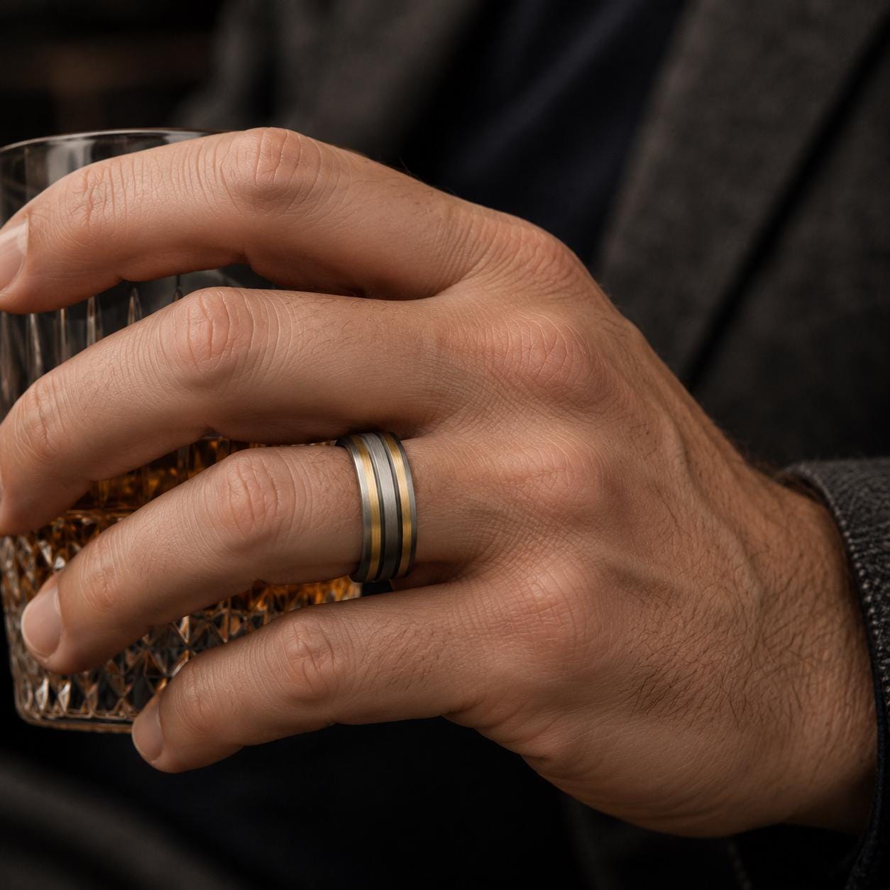 A close-up of a person's hand wearing a ring, holding a glass of what appears to be a beverage.