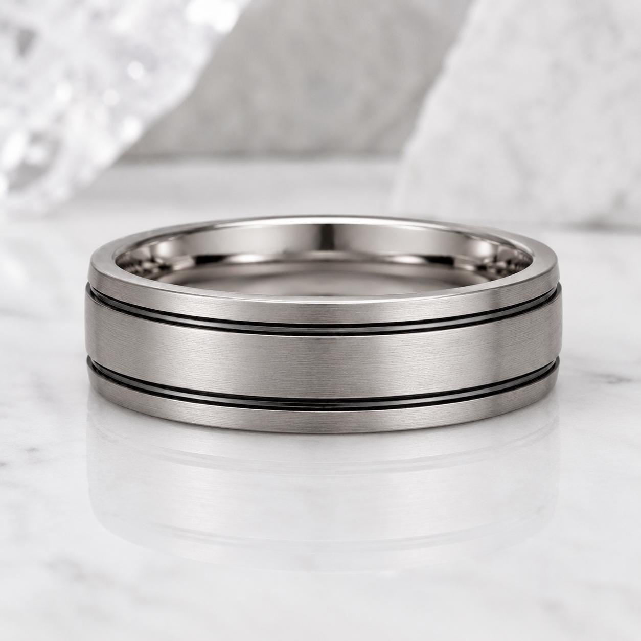 A silver-colored ring with a horizontal band design sits on a marble surface.